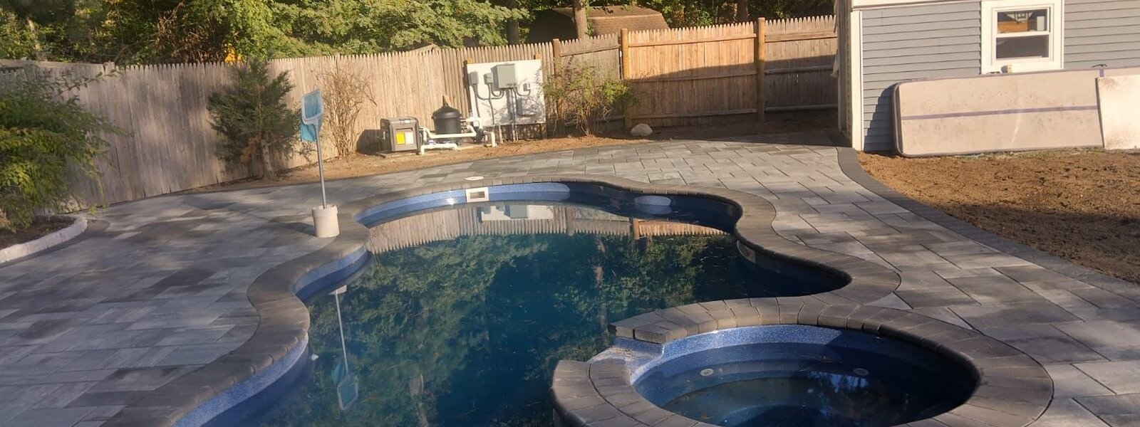 Freeform pool and spa surrounded by a wide paver deck