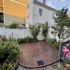Curved paver patio along a white privacy fence