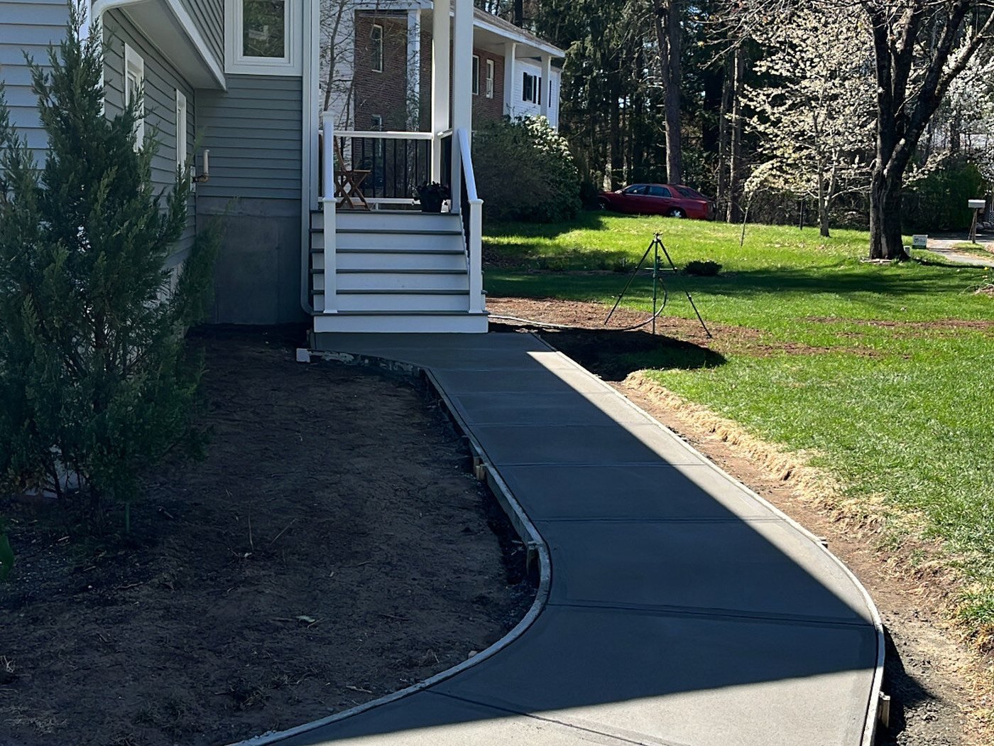 Fresh asphalt driveway curving past a concrete walkway and new lawn