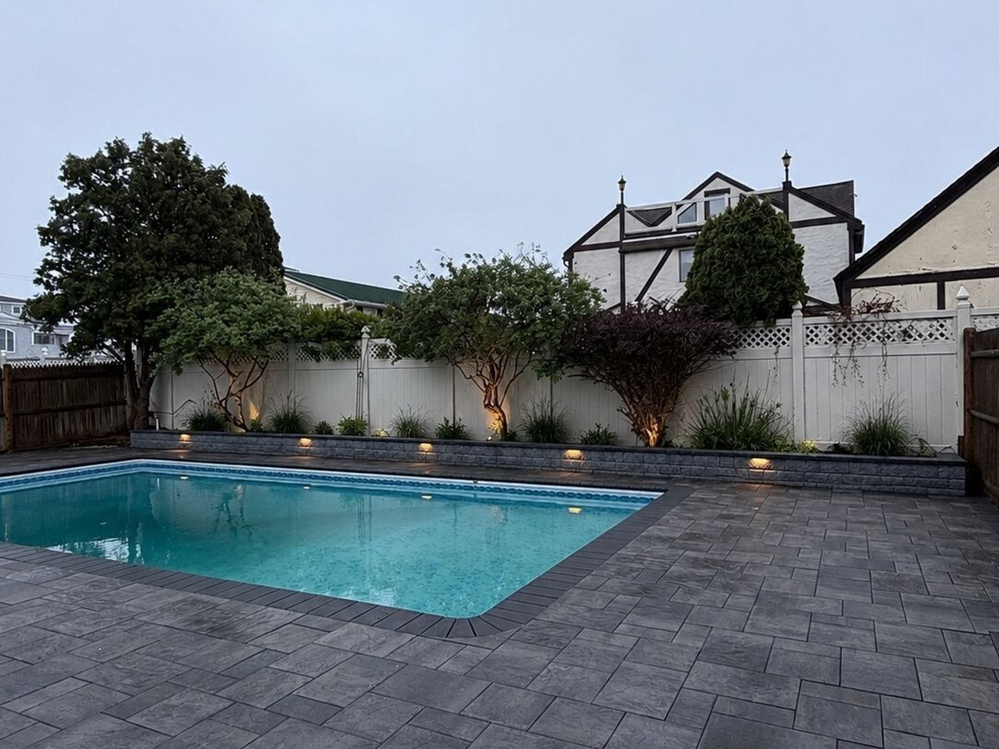Paver pool deck with landscape lighting along a white fence