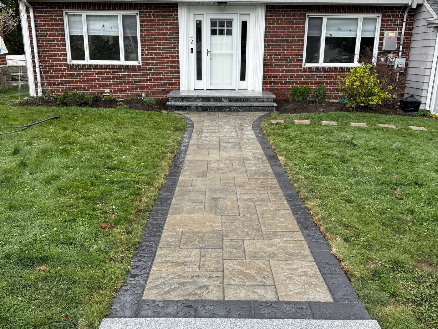 Paver walkway with a granite landing step leading to a brick home