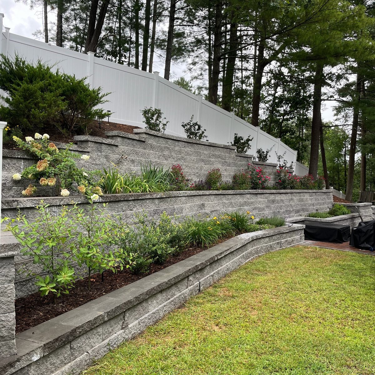 Tiered block retaining wall planted between a lawn and a fence